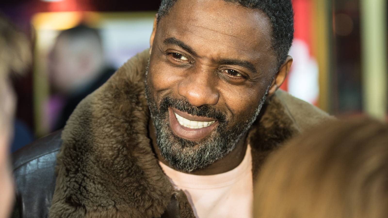 Idris Elba smiling in a fur collared coat at the Berlin International Film Festival in 2018