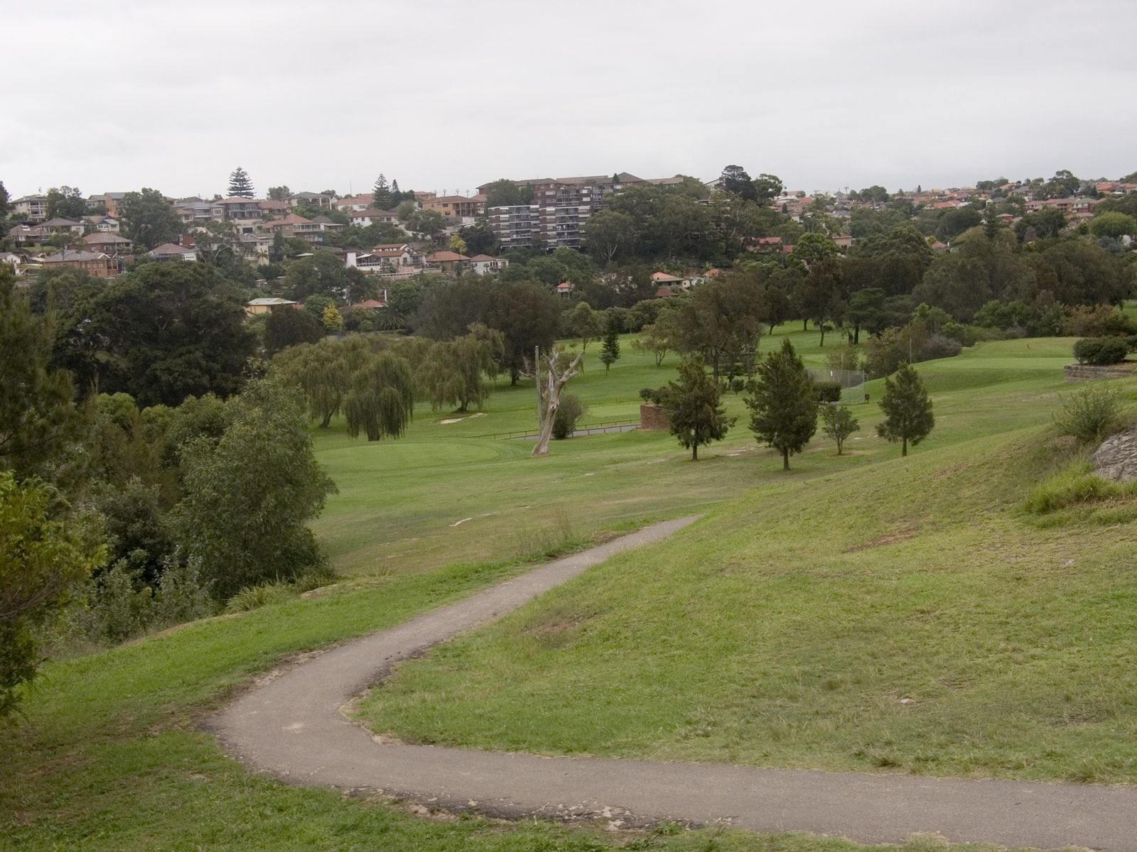 A golf course fairway lined with trees, with houses on the hills behind
