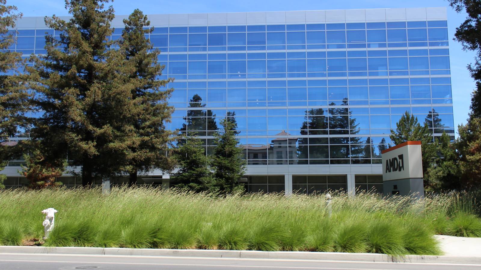 AMD's glass headquarters building at 2485 Augustine Drive in Santa Clara, California, with an AMD sign out front