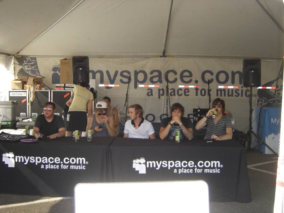 Anberlin members seated at a signing table under a tent