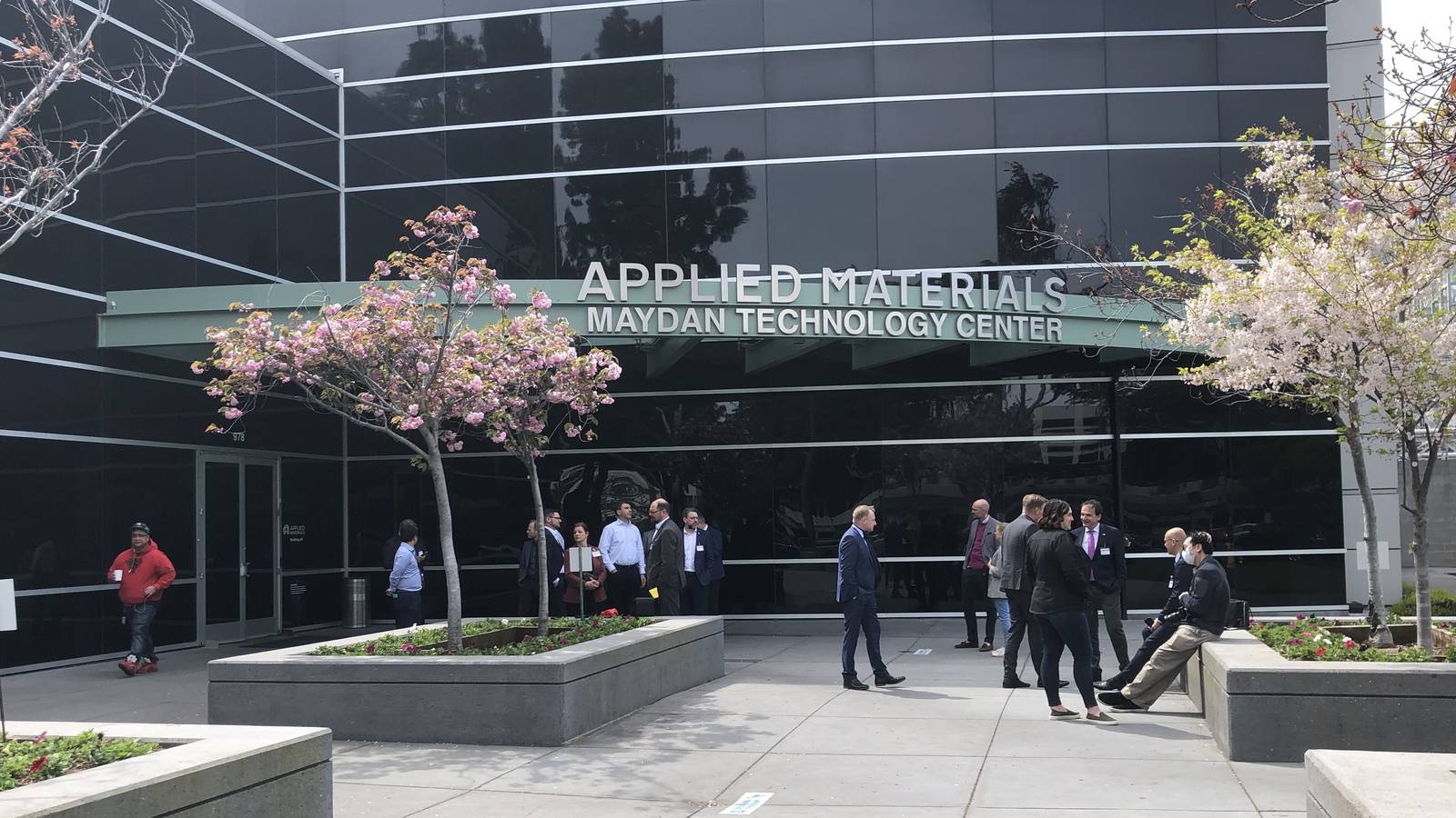 A glass office building with an Applied Materials Maydan Technology Center sign, with people walking outside