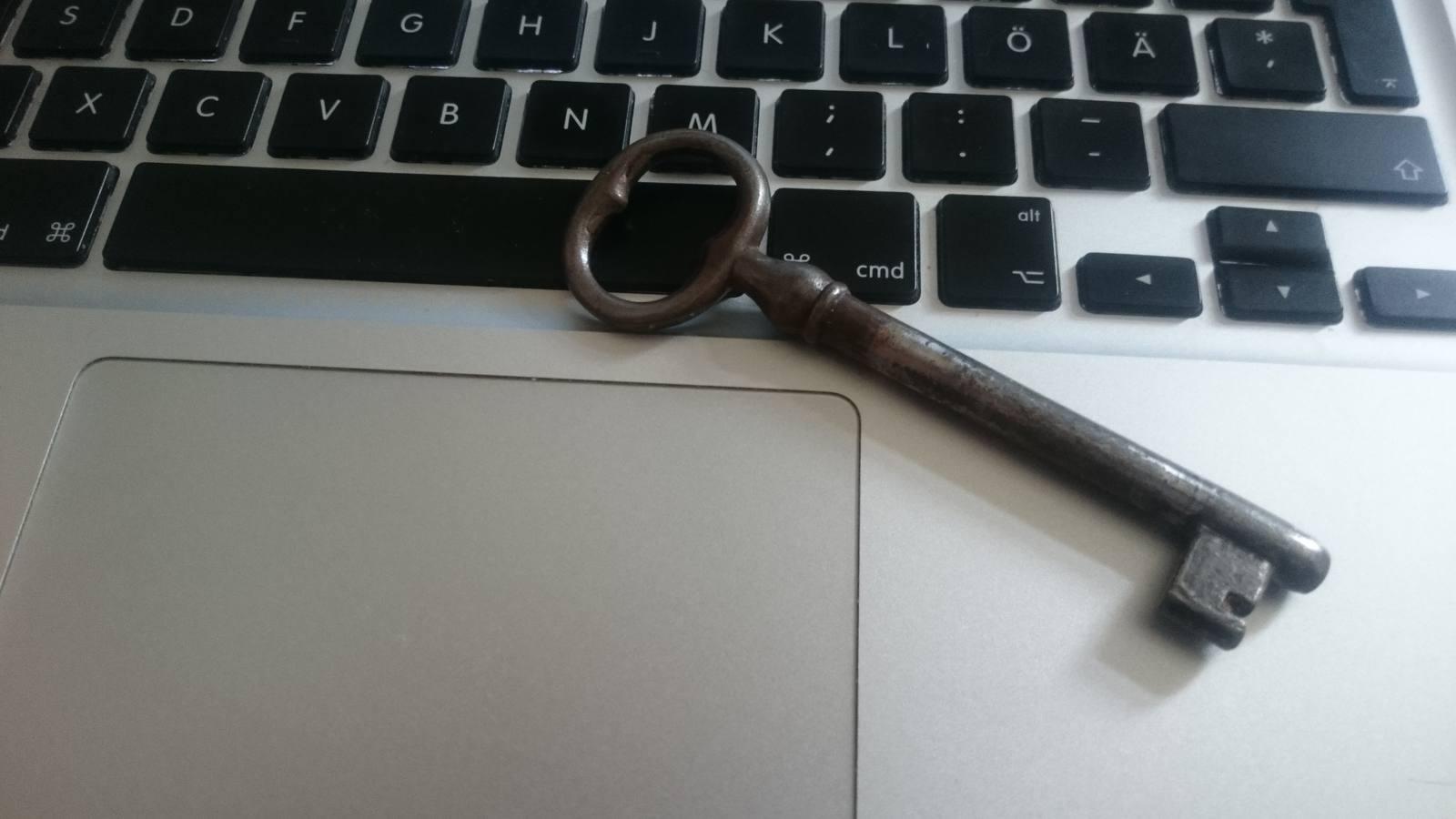 An old iron key resting on the silver keyboard and trackpad of a laptop