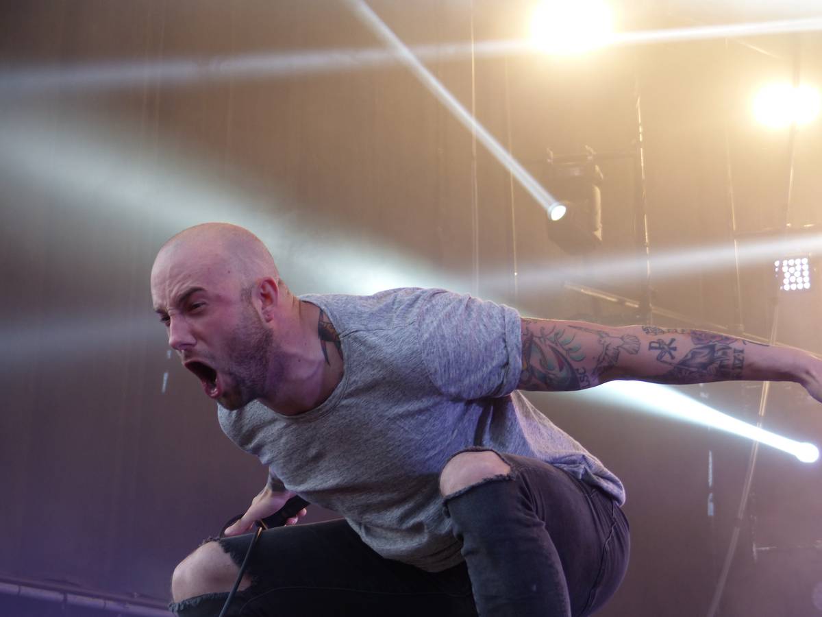August Burns Red singer Jake Luhrs crouching and shouting under white light beams