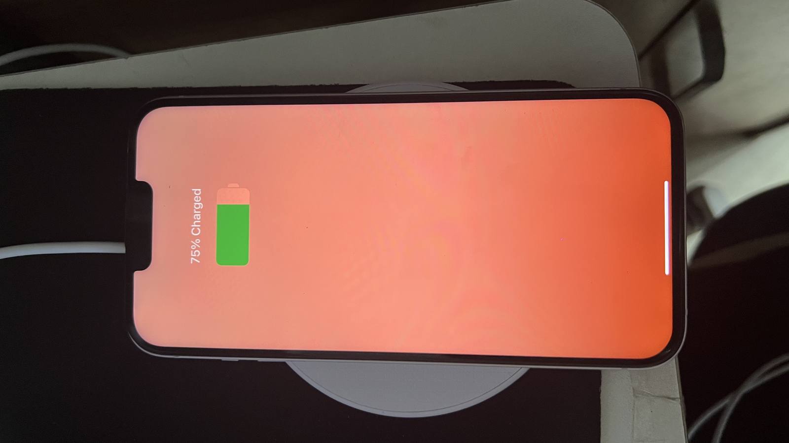 An iPhone lying on a round wireless charger, its screen showing a green battery icon at 75 percent charged