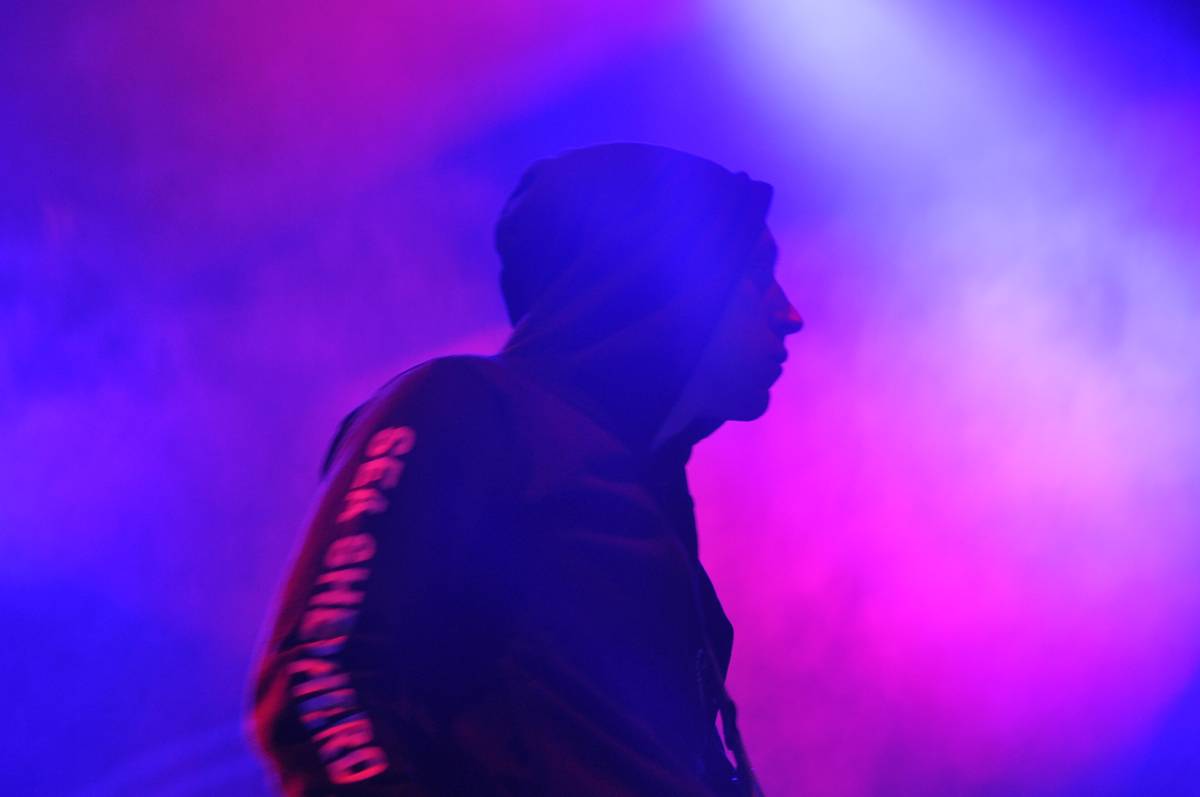 A hooded Boysetsfire member in silhouette against purple and pink stage haze