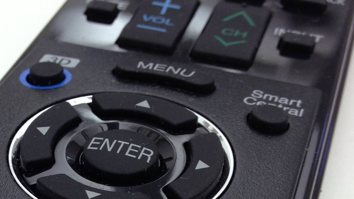 Close up of a black TV remote showing the menu, enter, volume and channel buttons