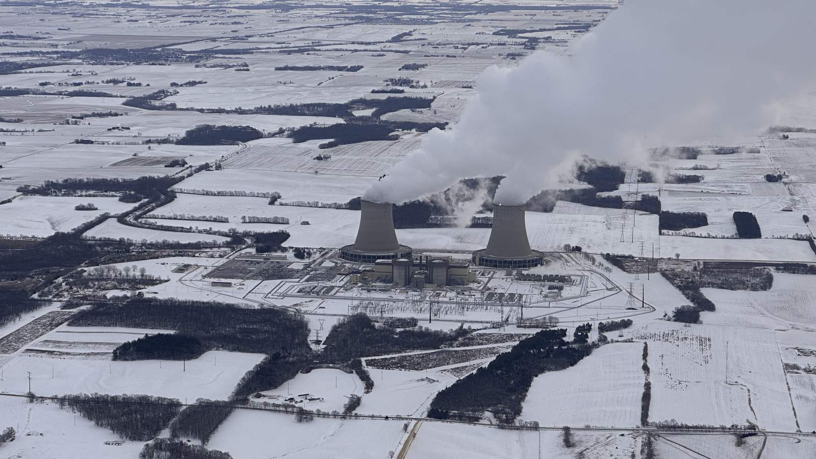 Aerial view of a nuclear plant's two cooling towers venting white plumes over flat, snow-covered Illinois farmland