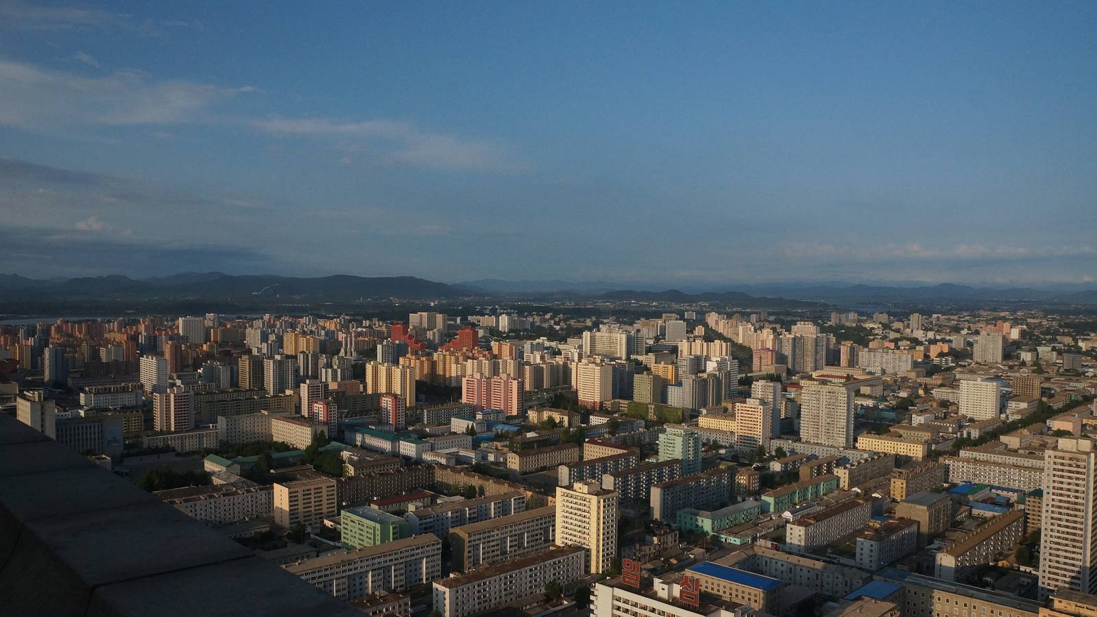 Apartment blocks across Pyongyang under a blue sky with hills on the horizon