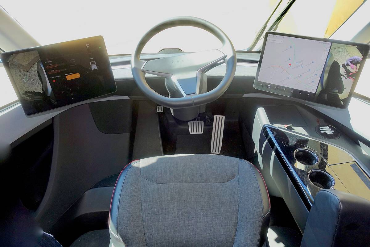 The inside of a Tesla Semi cab, with a central seat and a screen on each side of the steering wheel