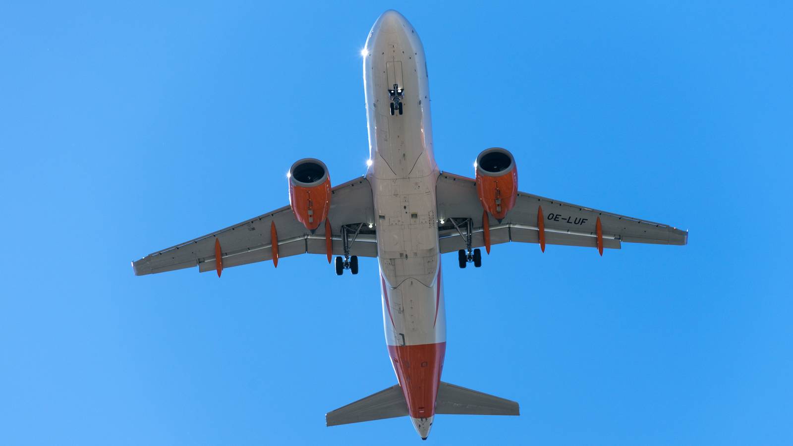 An easyJet Airbus A320neo with orange engines seen from below as it flies through a clear blue sky over Lisbon