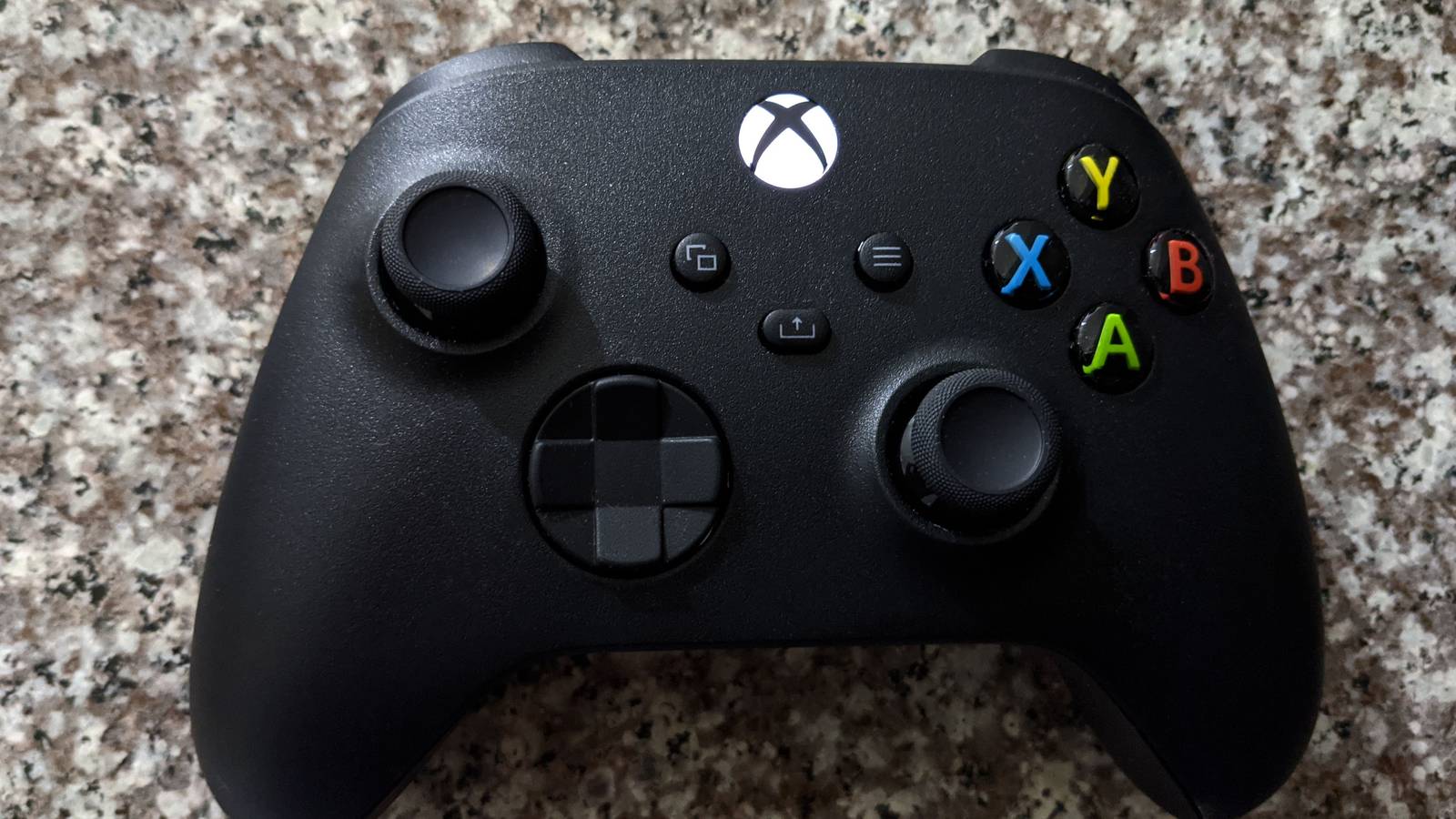 A black Xbox Series controller with coloured face buttons resting on a speckled granite surface