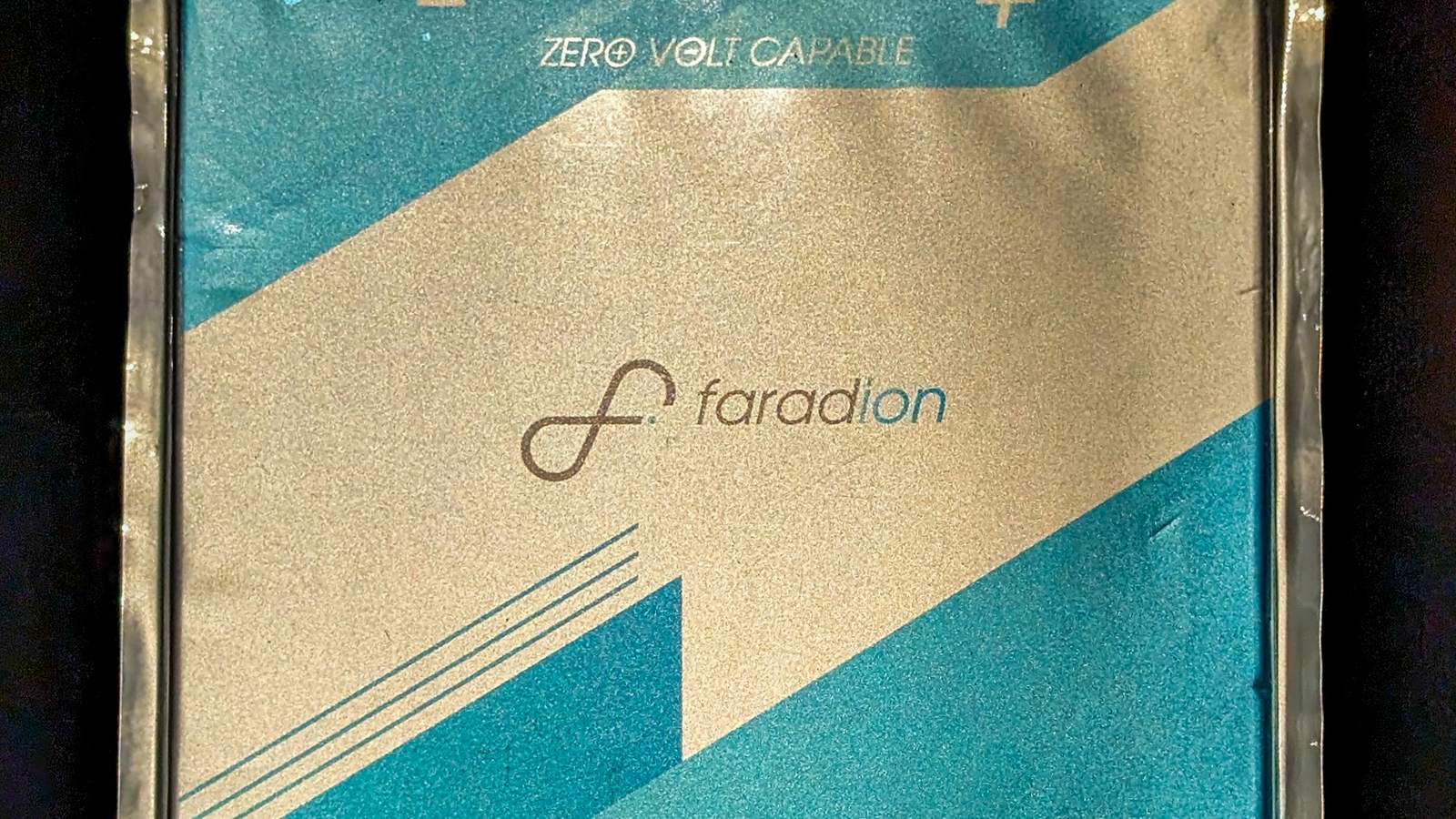 Close up of a Faradion sodium ion battery cell, a flat pouch with teal and silver branding