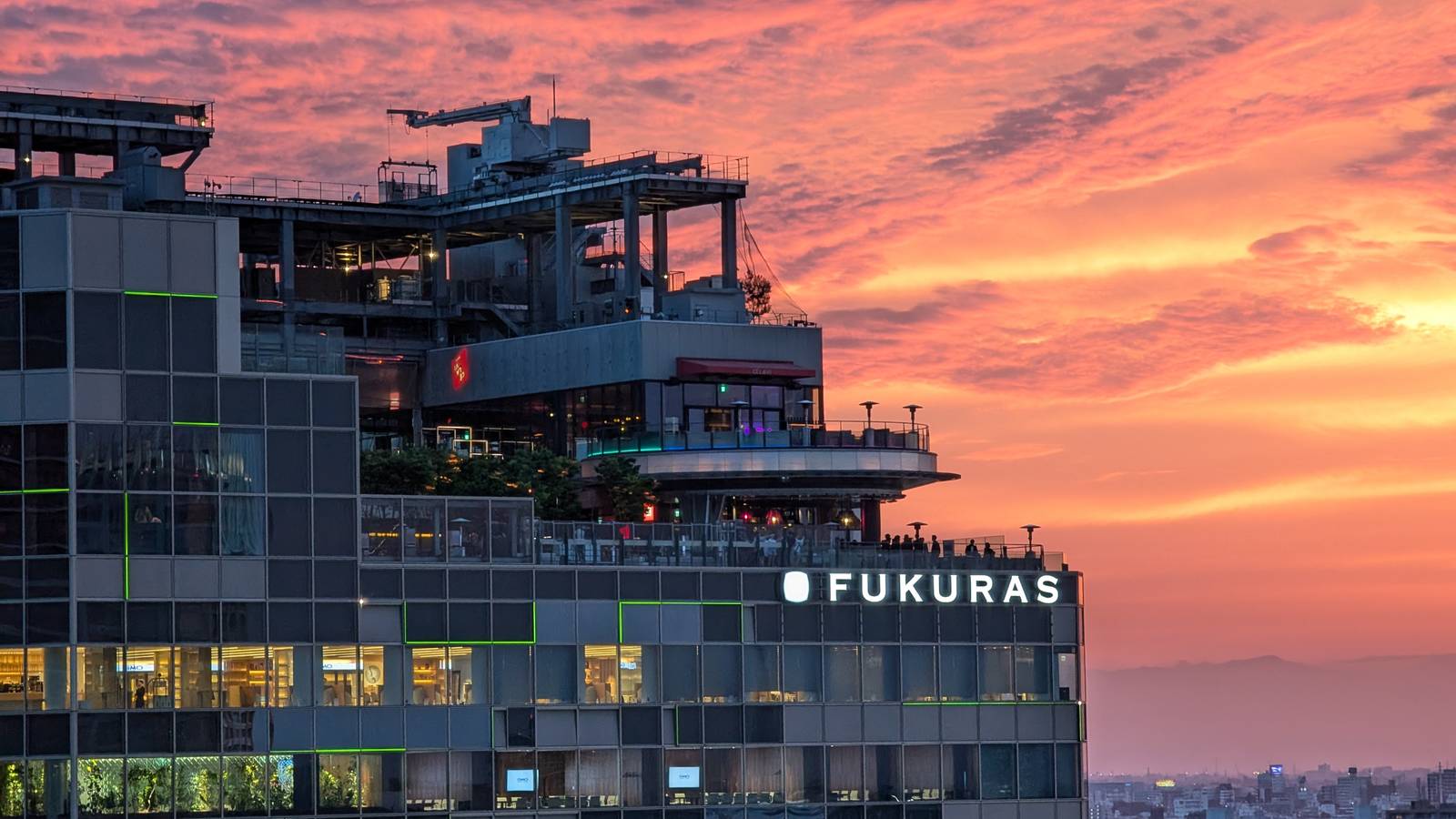 The Shibuya Fukuras building, home of GMO Internet Group, under a pink and orange evening sky in Tokyo
