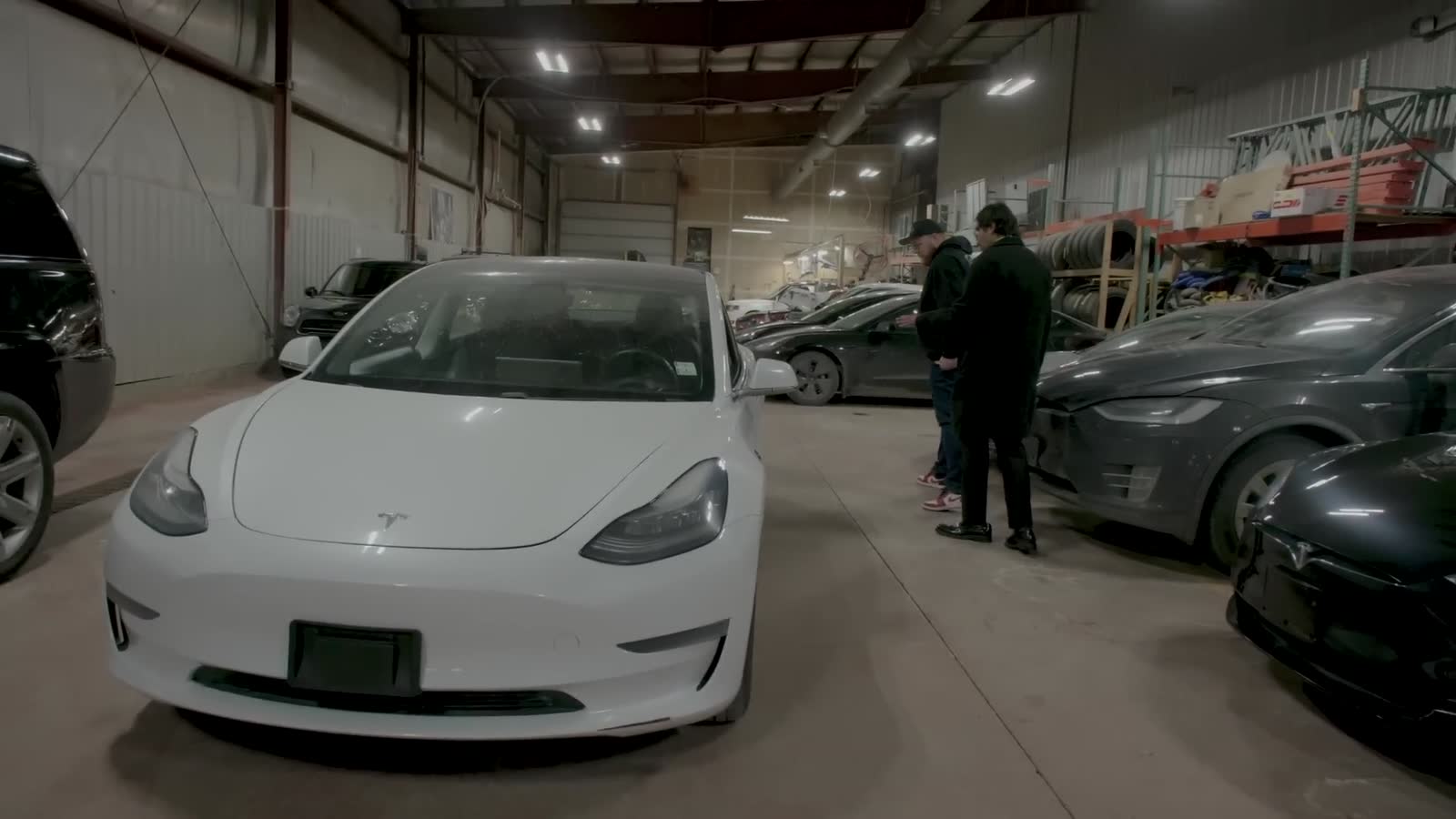White Tesla Model 3 with 600,000 km parked in a used car dealer's indoor lot, seen from the front