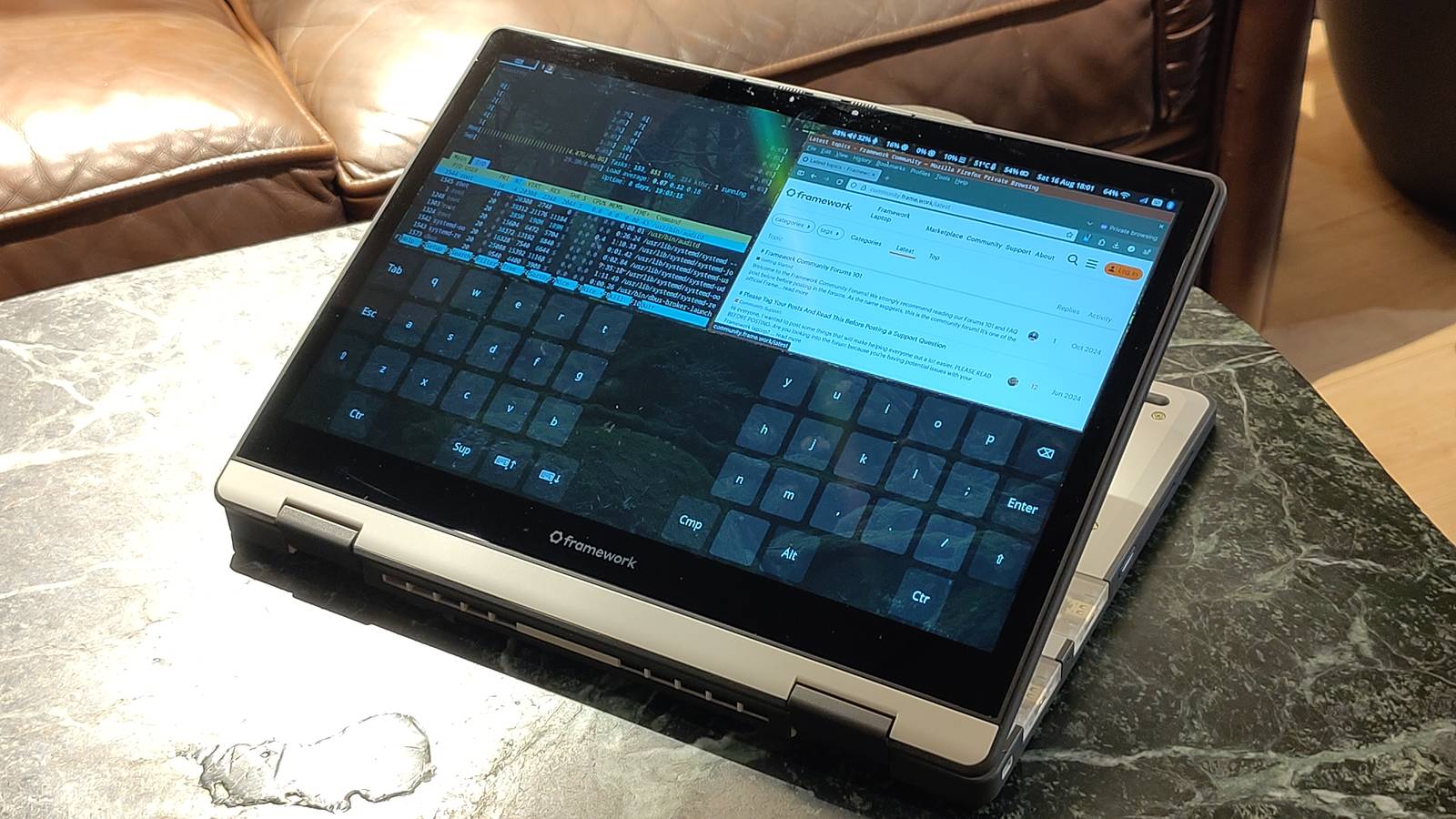 A Framework laptop folded into tablet mode on a marble table, its screen showing a web browser