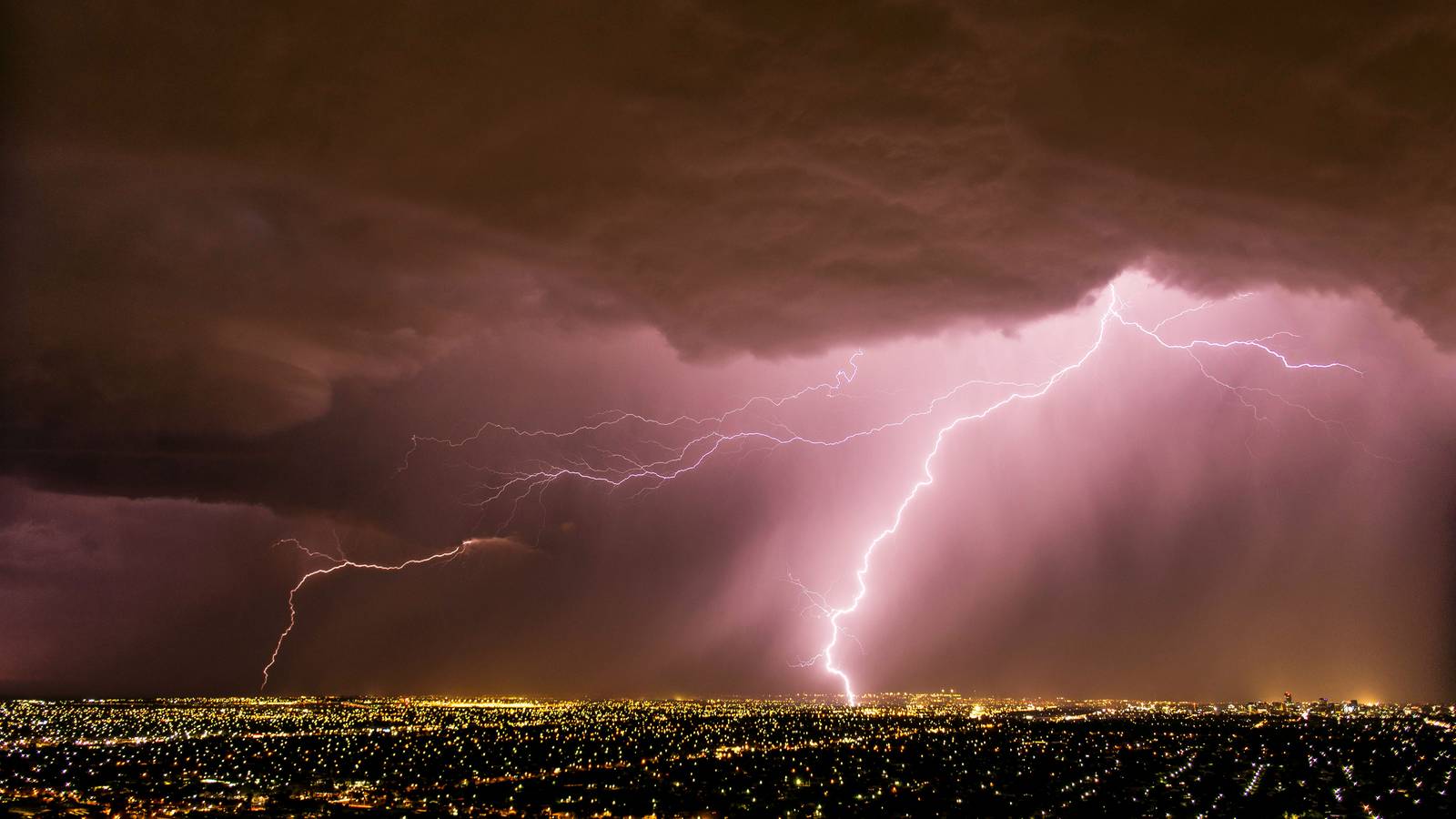 Lightning strikes from a dark storm cell over the lights of suburban Adelaide at night