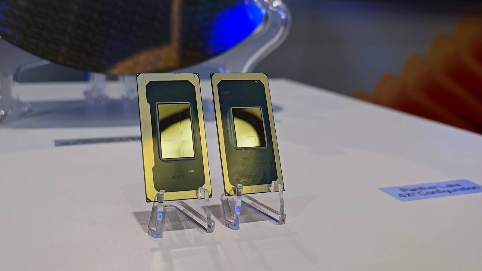 Two Intel Panther Lake processor packages on stands in front of a silicon wafer