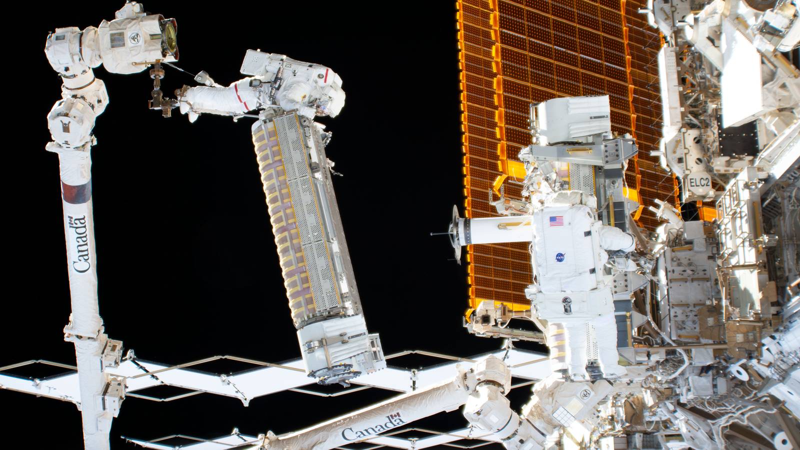 Astronauts on a spacewalk install a rolled up solar array on the International Space Station using the Canadarm2 robot arm