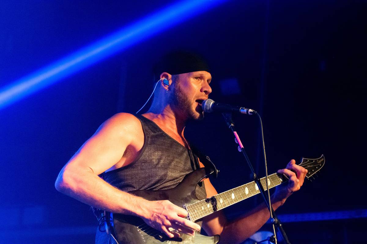 A Killswitch Engage guitarist singing into a microphone under blue light
