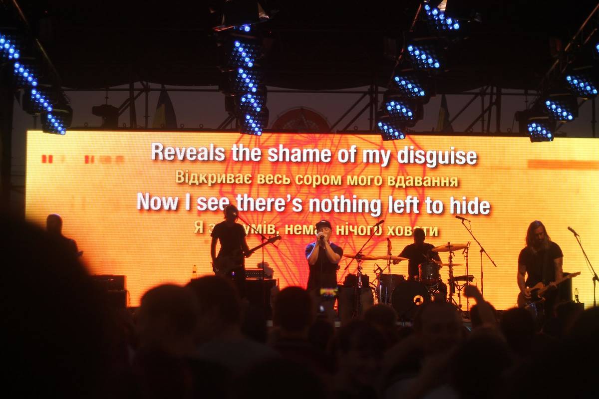 Kutless in silhouette in front of a screen showing song lyrics in English and Ukrainian