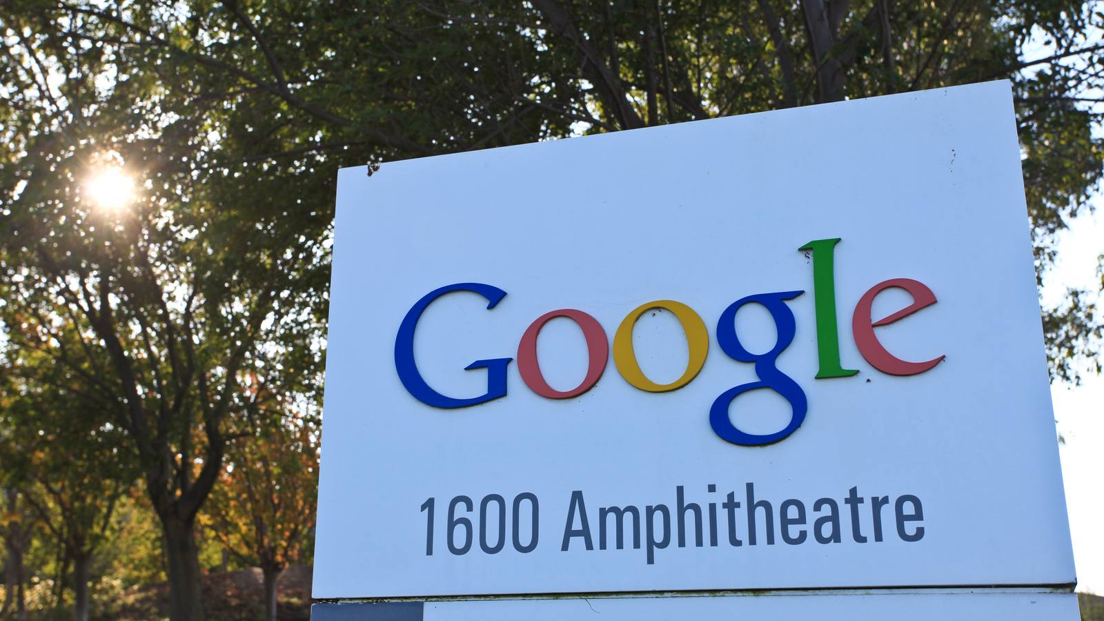 A white Google sign reading 1600 Amphitheatre in front of trees with the sun shining through the leaves