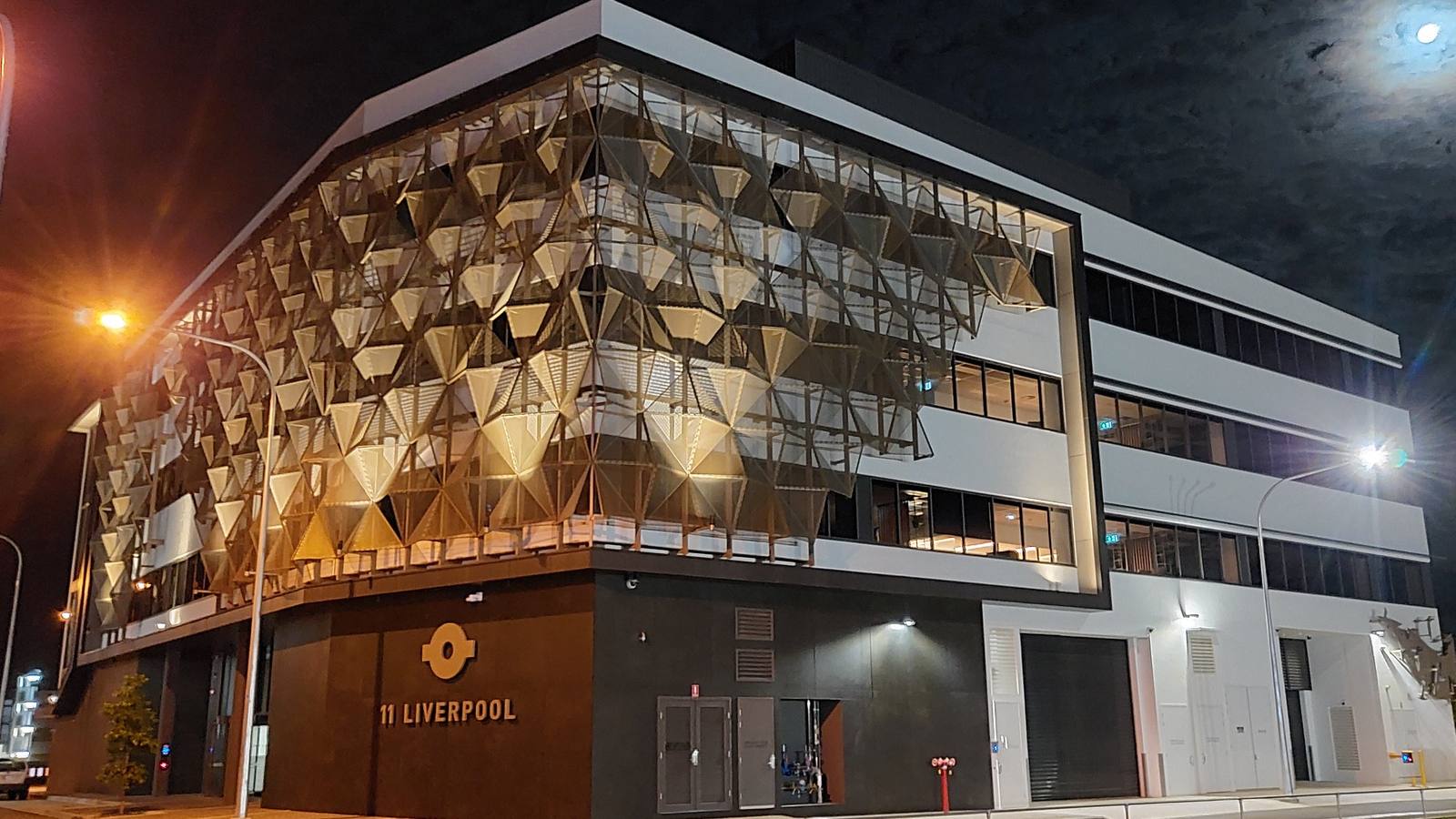 The ATO office at 11 Liverpool Lane in Townsville lit up at night, with a gold patterned facade and street lights