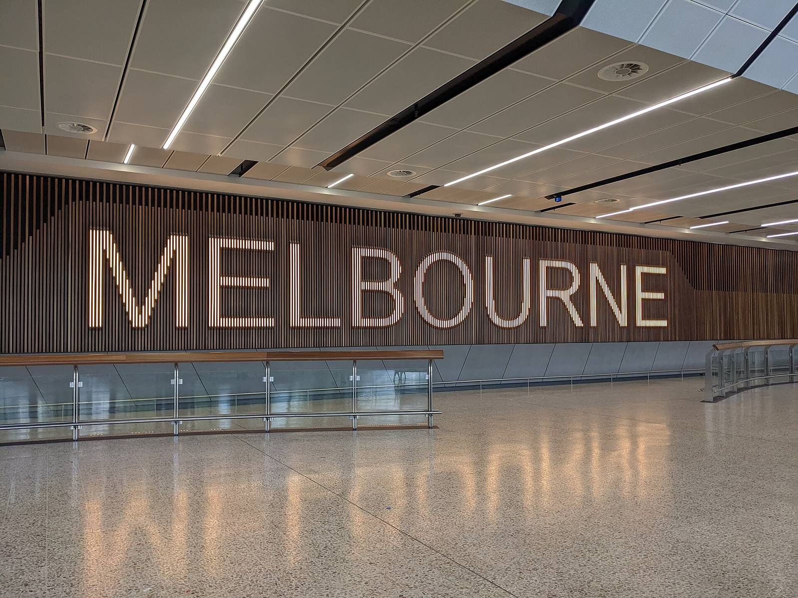 The empty international arrivals hall at Melbourne Airport with the word Melbourne on a timber wall