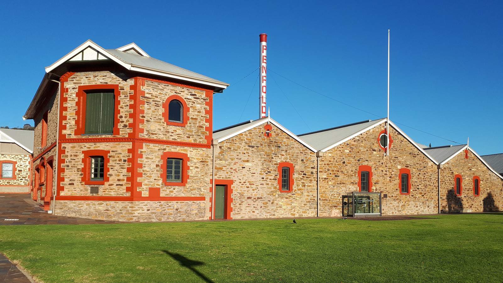 Red trimmed bluestone winery buildings and a tall chimney at Penfolds Magill Estate in the Adelaide foothills
