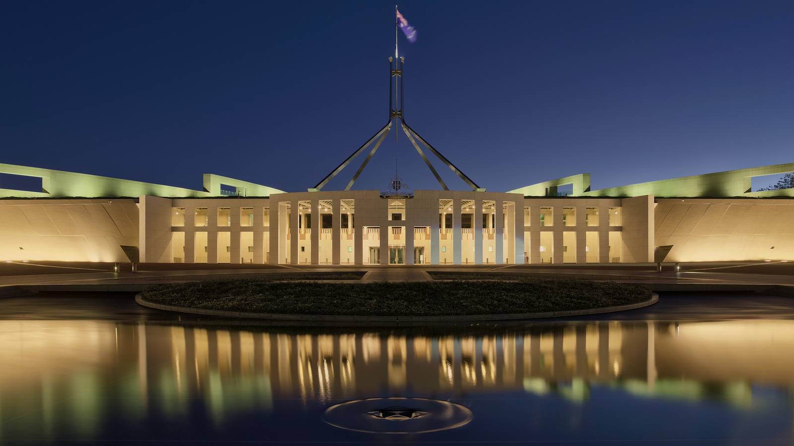 Parliament House in Canberra lit up at blue hour, reflected in the forecourt pool