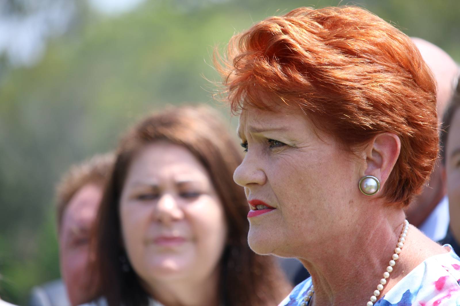 One Nation leader Pauline Hanson speaking outdoors, with people blurred behind her