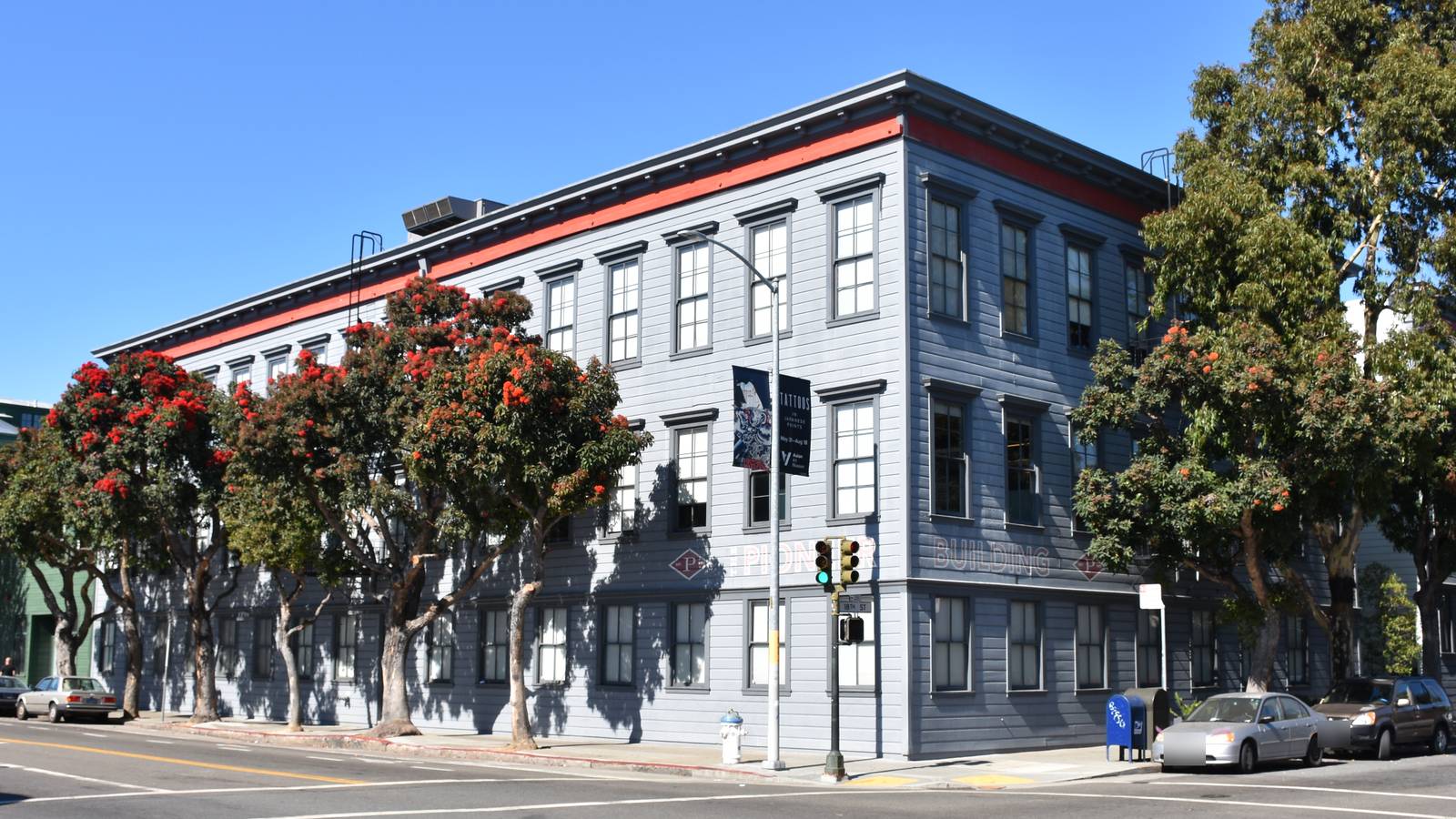 The grey three storey Pioneer Building on 18th Street in San Francisco, with red flowering trees along the pavement