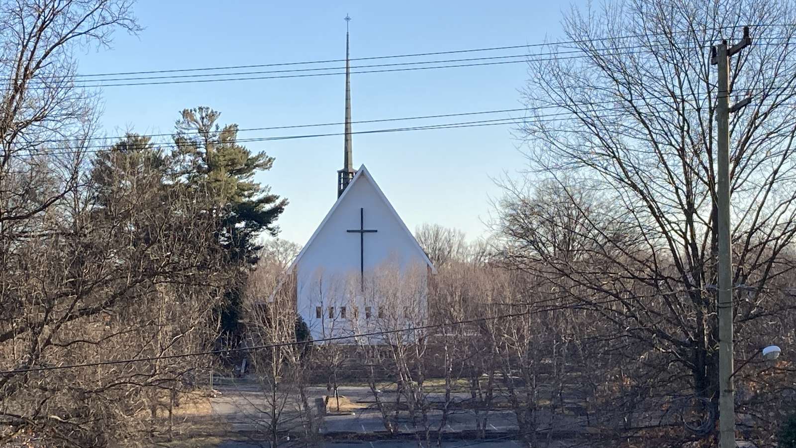 A white church with a tall spire and a black cross, seen behind bare winter trees in Maryland