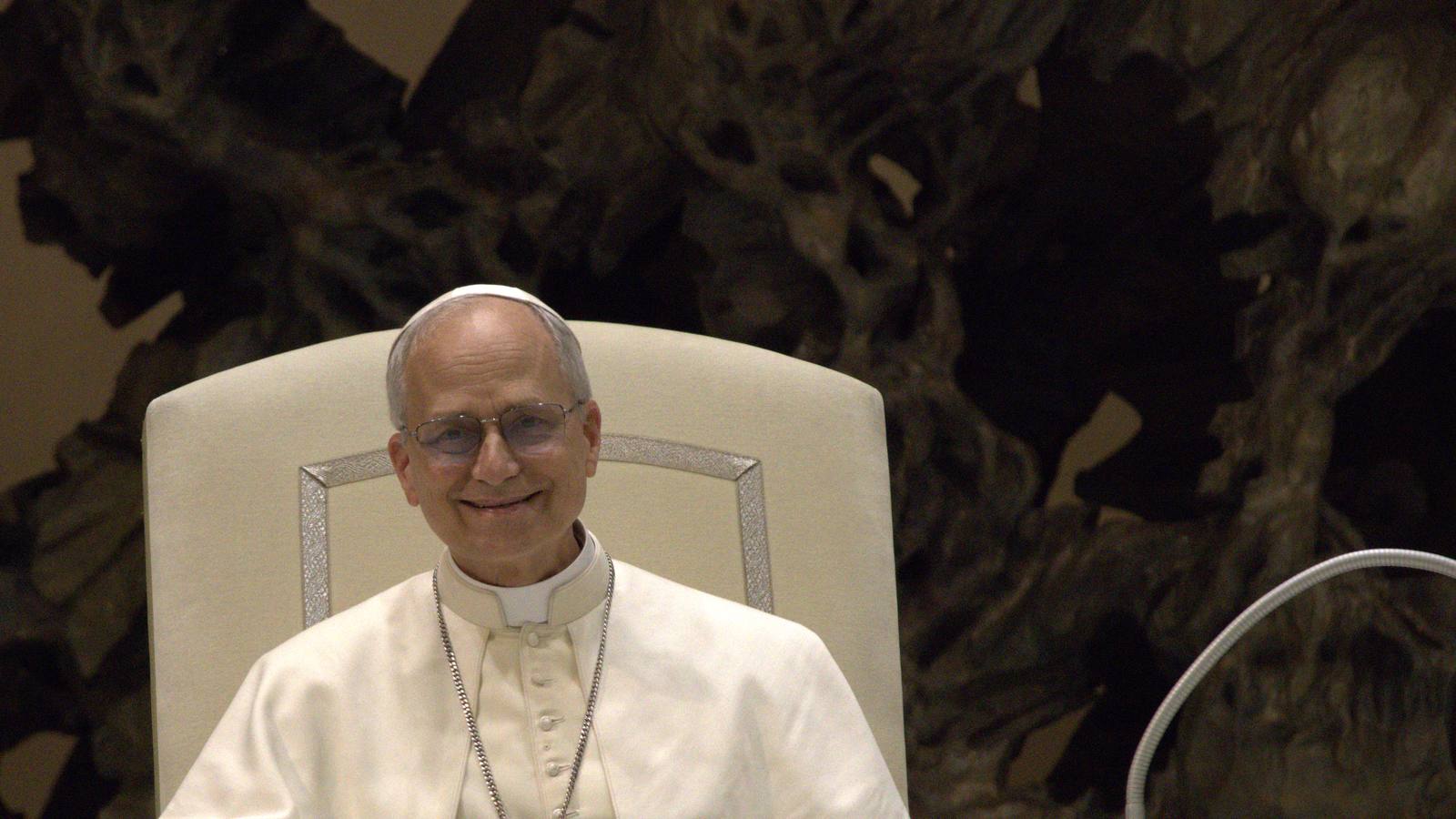 Pope Leo XIV smiling as he sits in a white chair during an audience with the media at the Vatican