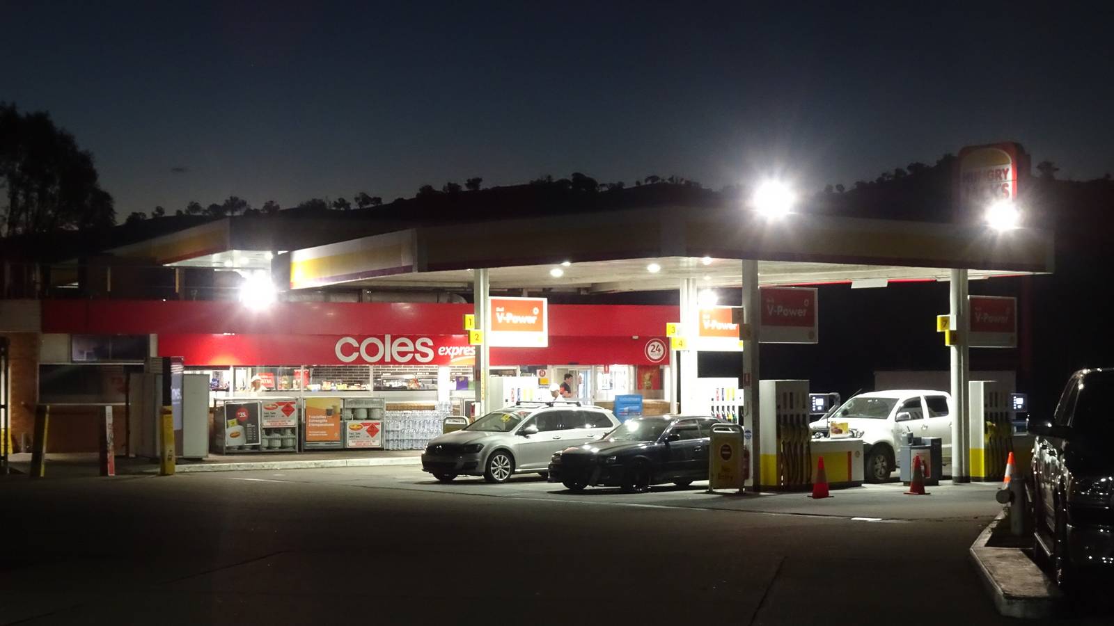 Petrol bowsers and a lit service station canopy at night