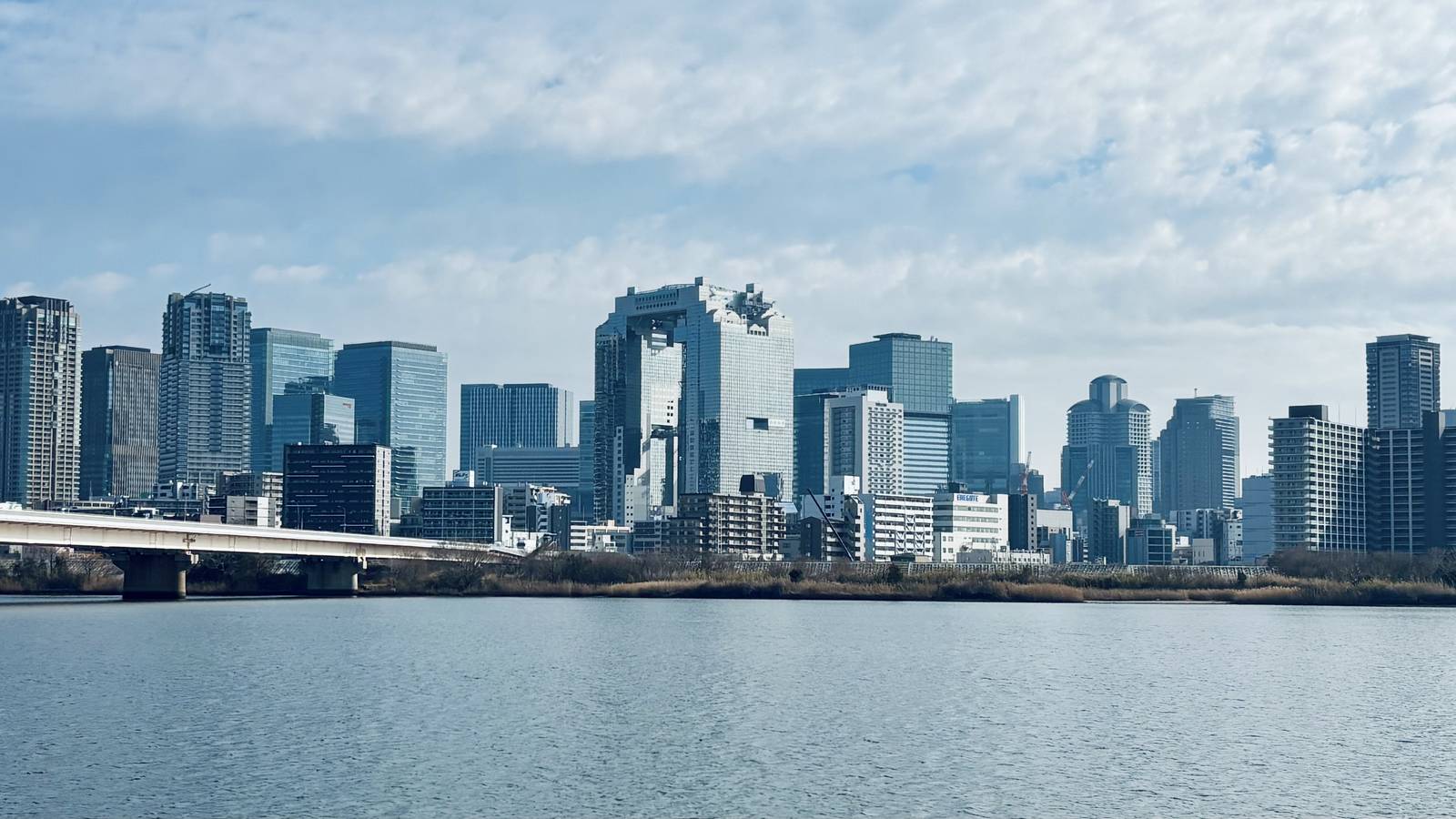 The Umeda skyline in Osaka seen across the wide Yodo River under a partly cloudy sky