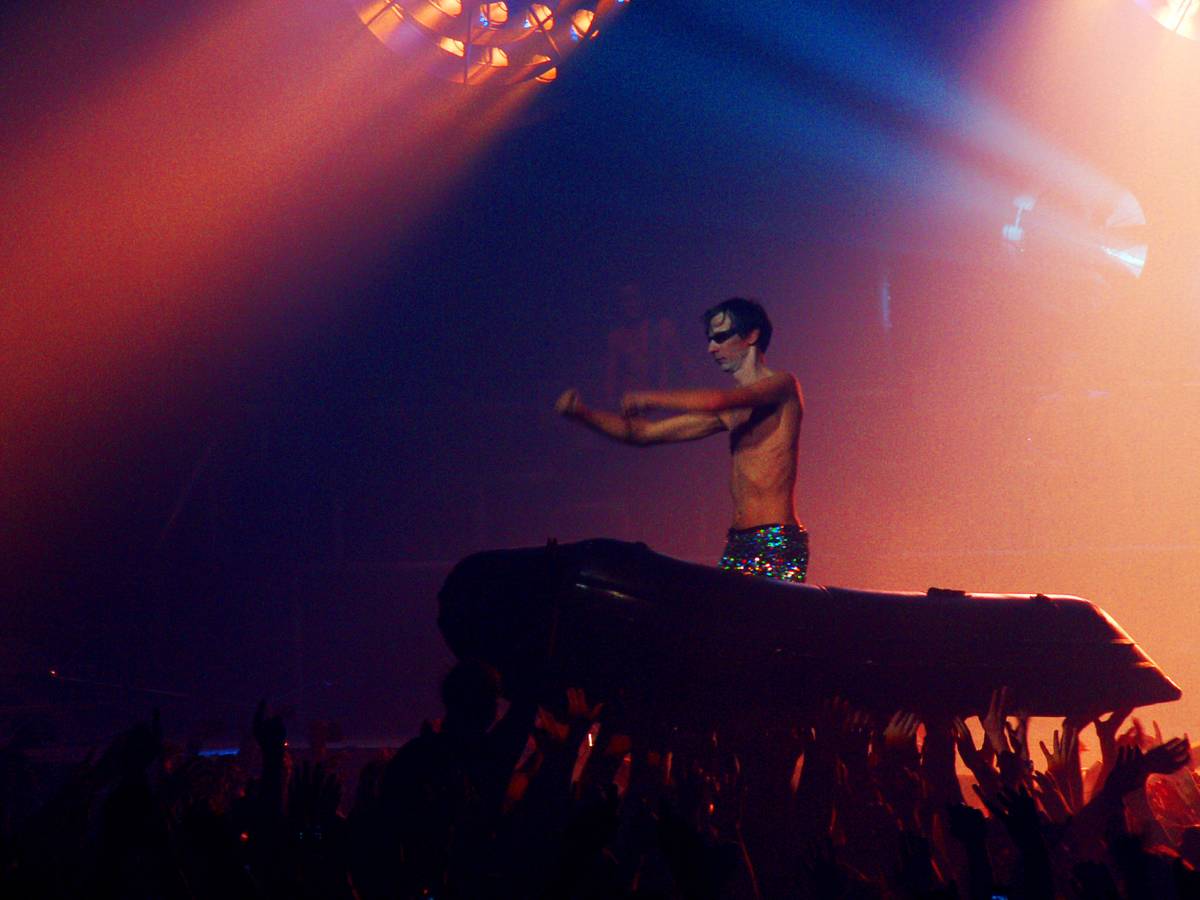 Rammstein keyboardist Flake Lorenz, shirtless, standing in an inflatable boat over the crowd