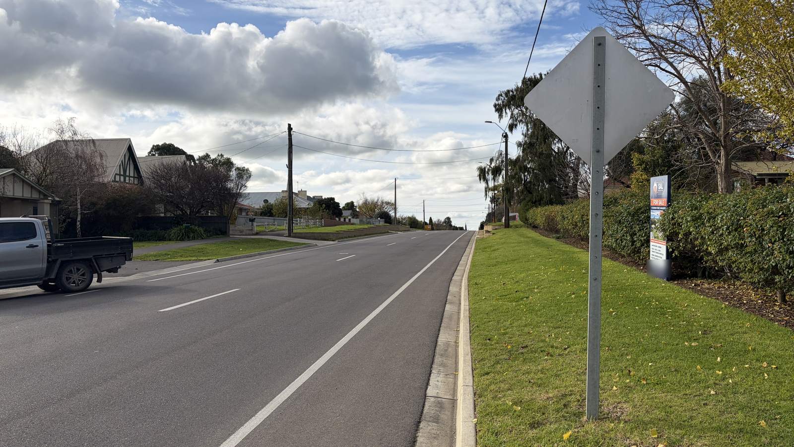 A quiet road past houses, gardens and a for sale sign in Naracoorte, South Australia, under a cloudy sky