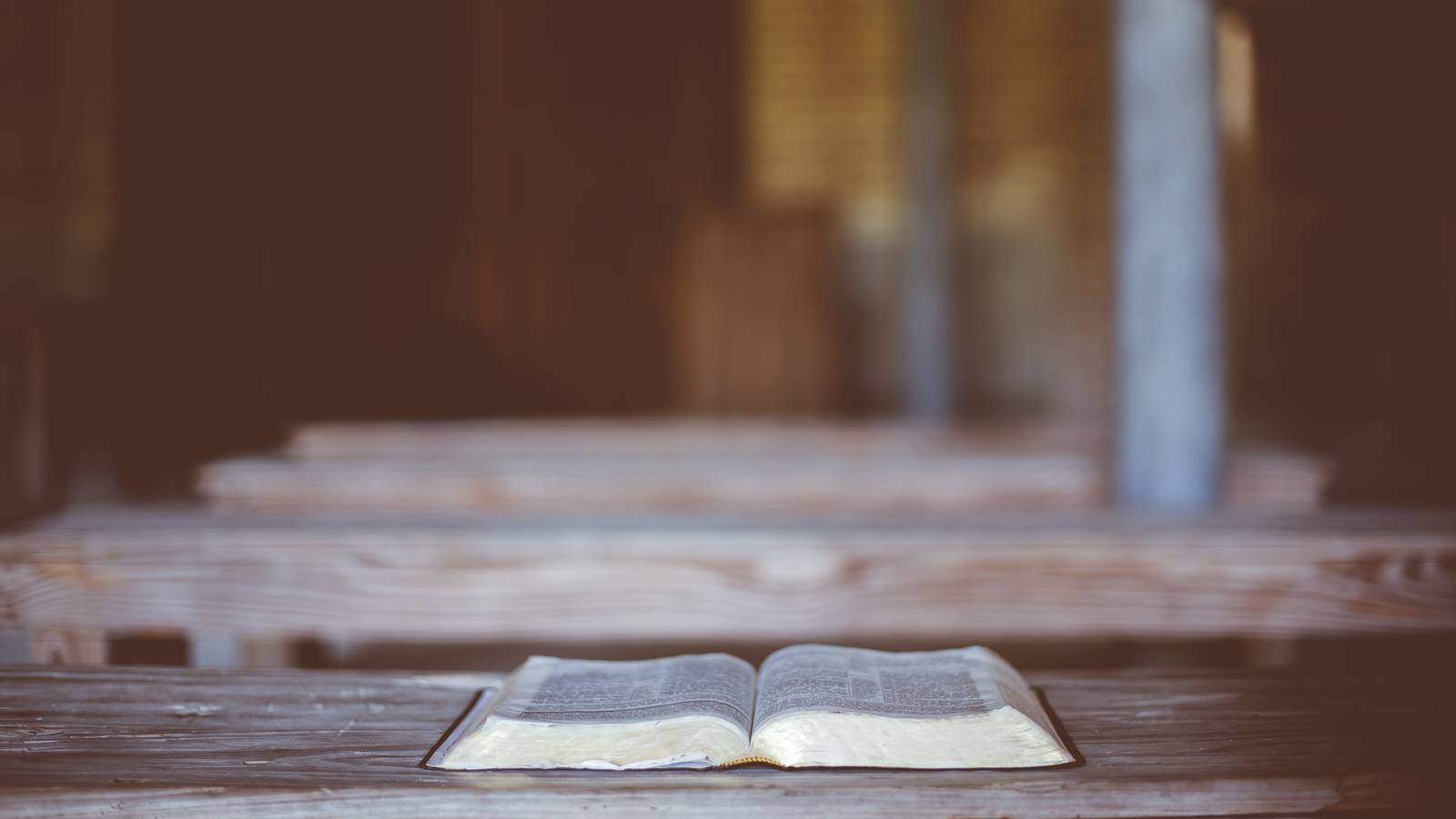 An open Bible resting on a wooden church pew with empty pews blurred behind it