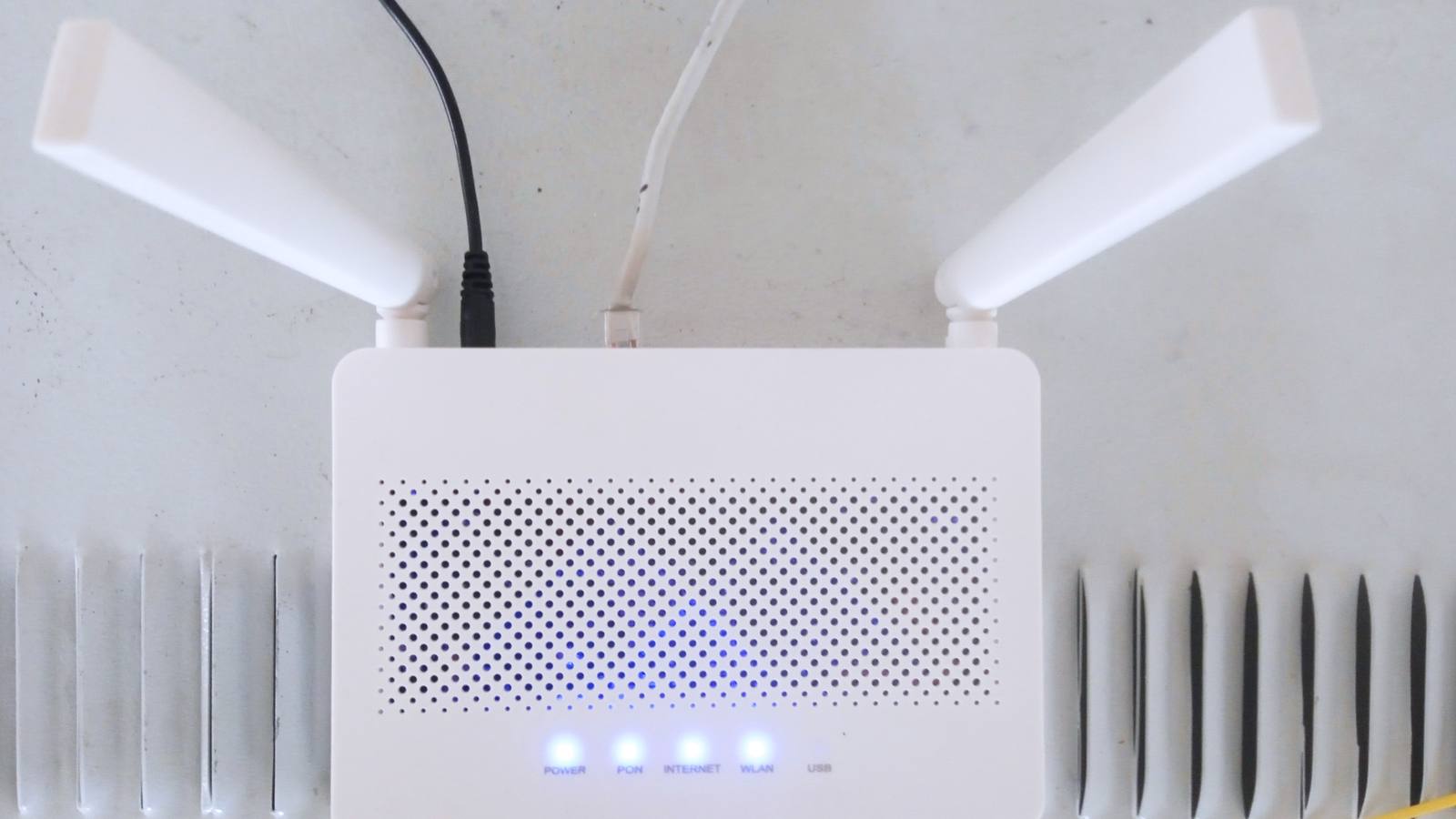 A white home WiFi router with two antennas and four blue status lights glowing, cables plugged into the top