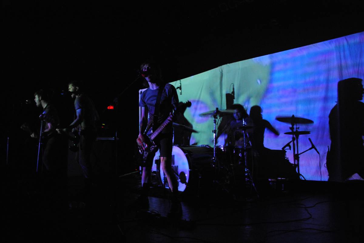 Showbread playing on a dark stage with a projection behind