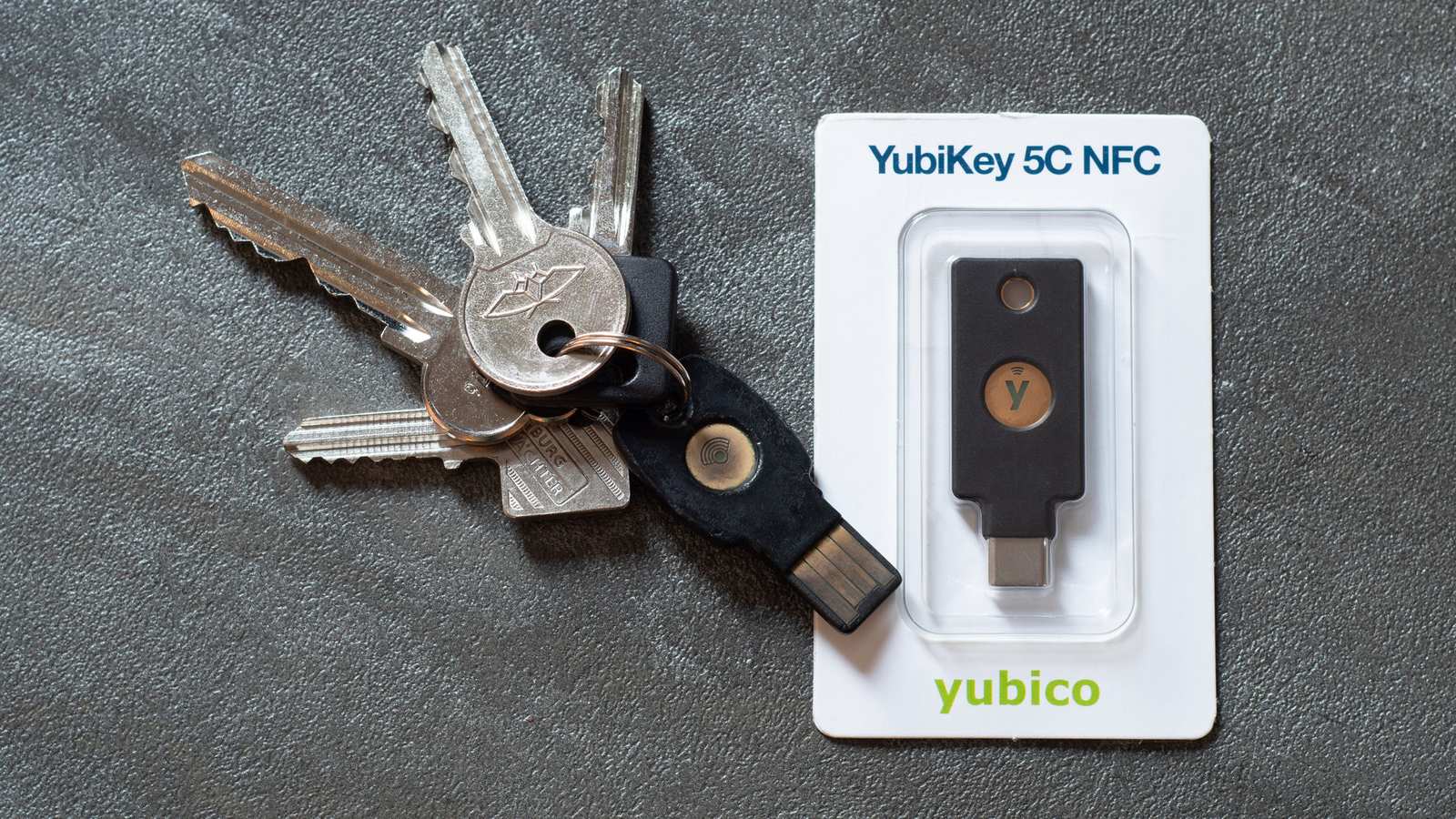 A YubiKey 5C NFC security key in its retail pack next to a bunch of house keys with another YubiKey attached