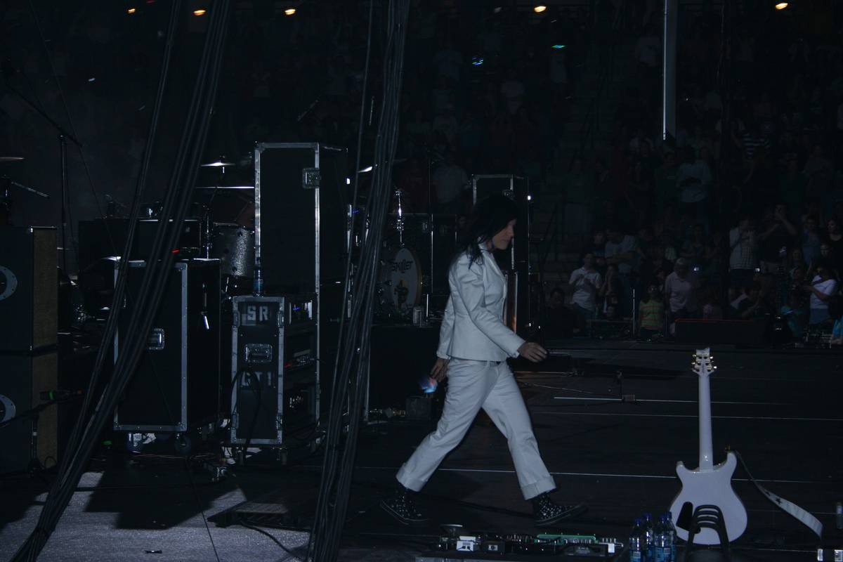 A Skillet member in a white suit walking across a dim stage past a guitar on a stand