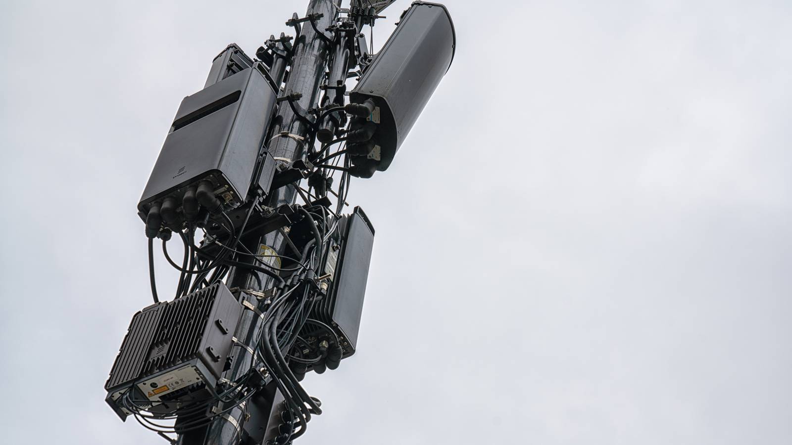 Cellular antenna panels and radio units mounted on a cell tower against a grey sky