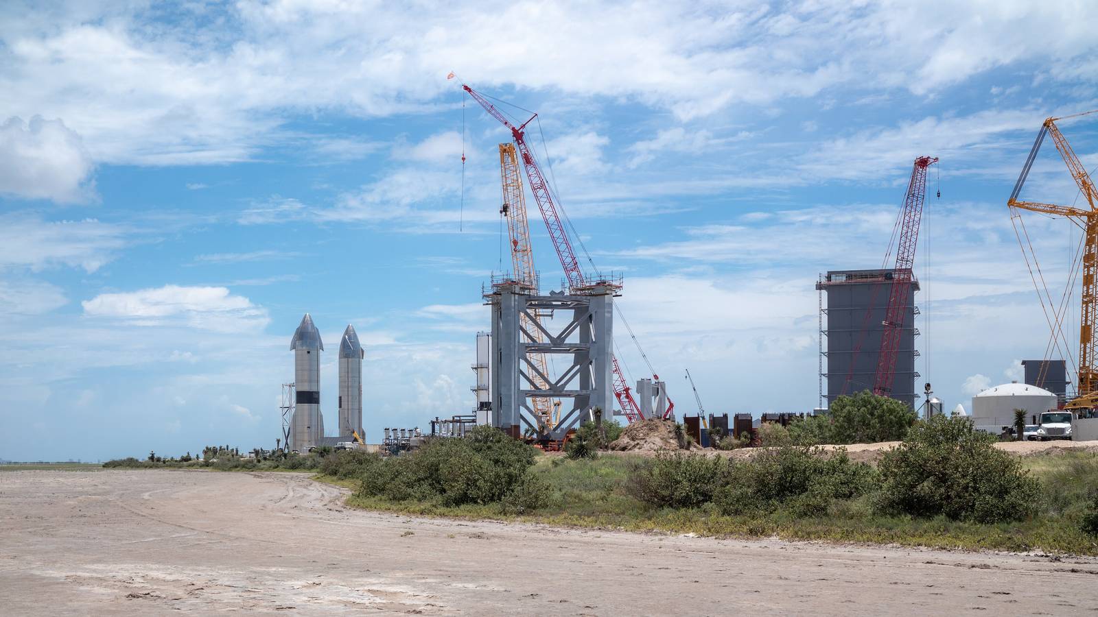 Two Starship prototypes stand beside a launch tower under construction at Starbase on the Texas coast