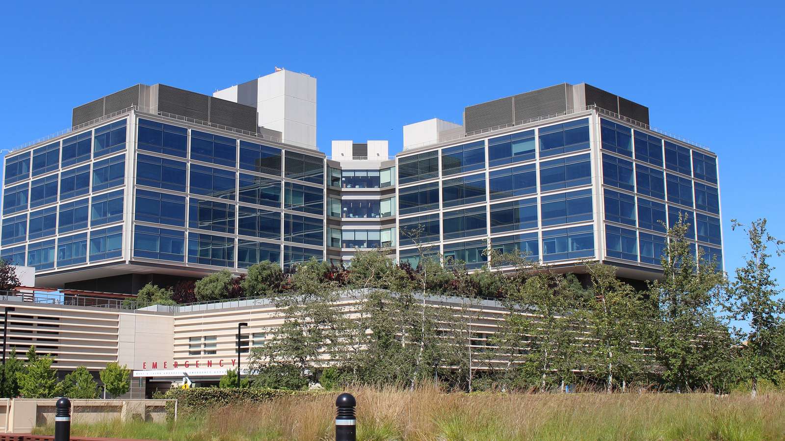 The glass and steel towers of the new Stanford Hospital under a clear blue sky, with trees and landscaping in front