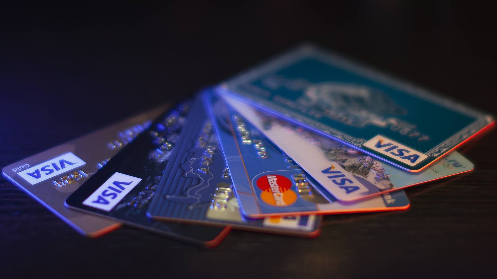 A fan of Visa and Mastercard credit cards lying on a dark wooden table under blue light