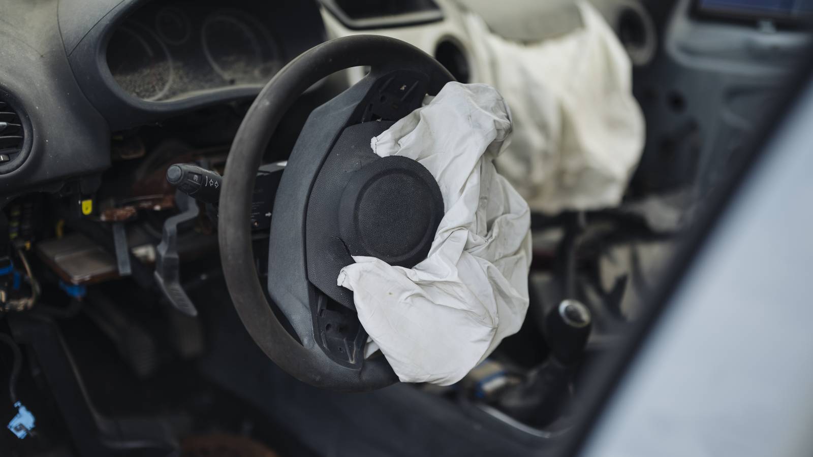 A deployed airbag hanging from the steering wheel of an old abandoned car