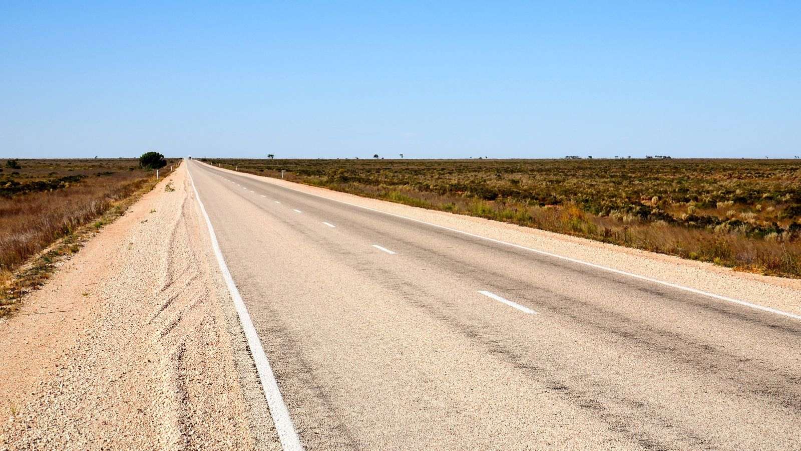 A long, straight two-lane highway running east to a flat horizon across low scrub on the Nullarbor Plain under a clear sky