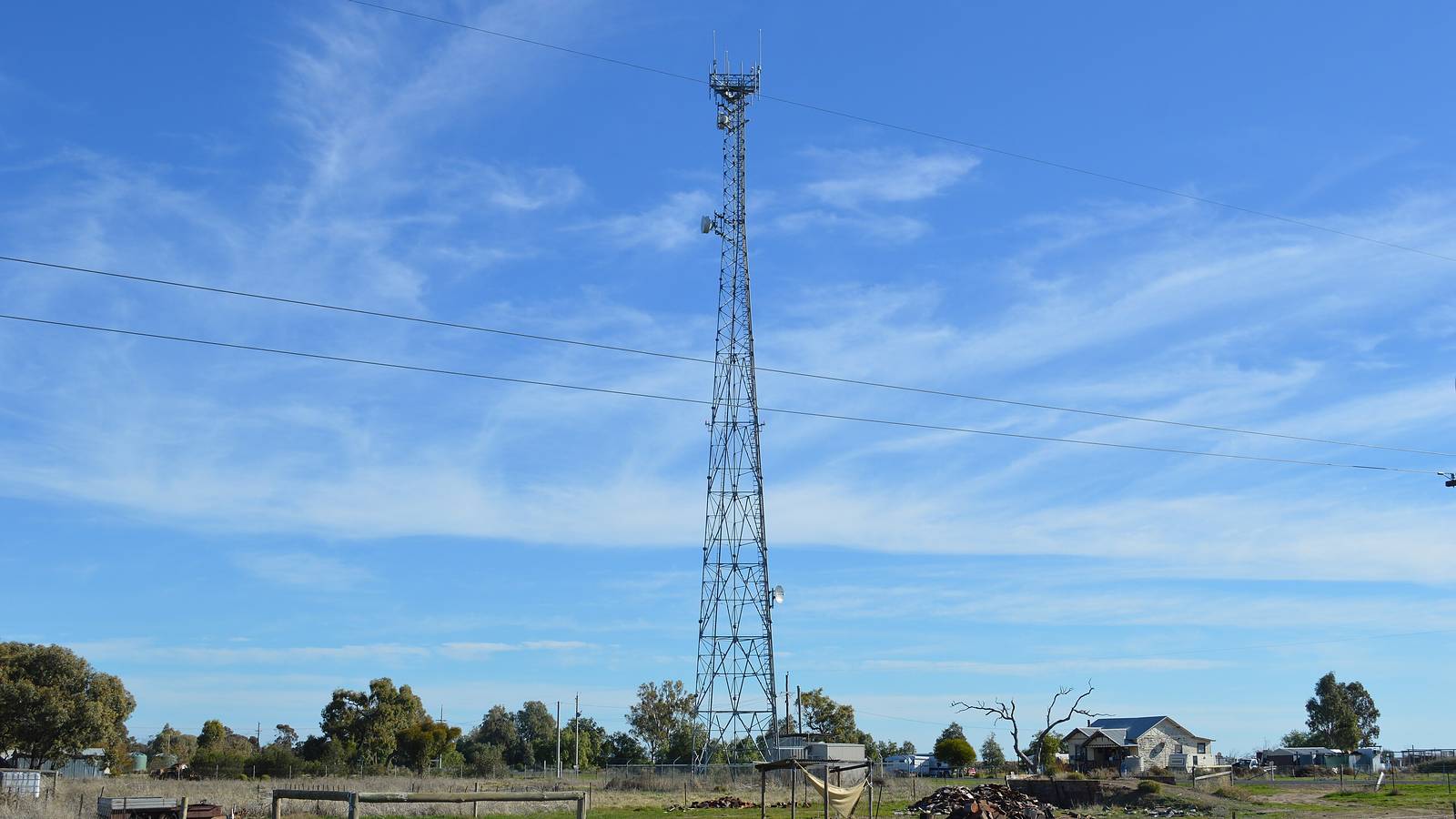A tall lattice telecommunications tower with antennas rising over paddocks and a house in Oxley, regional NSW