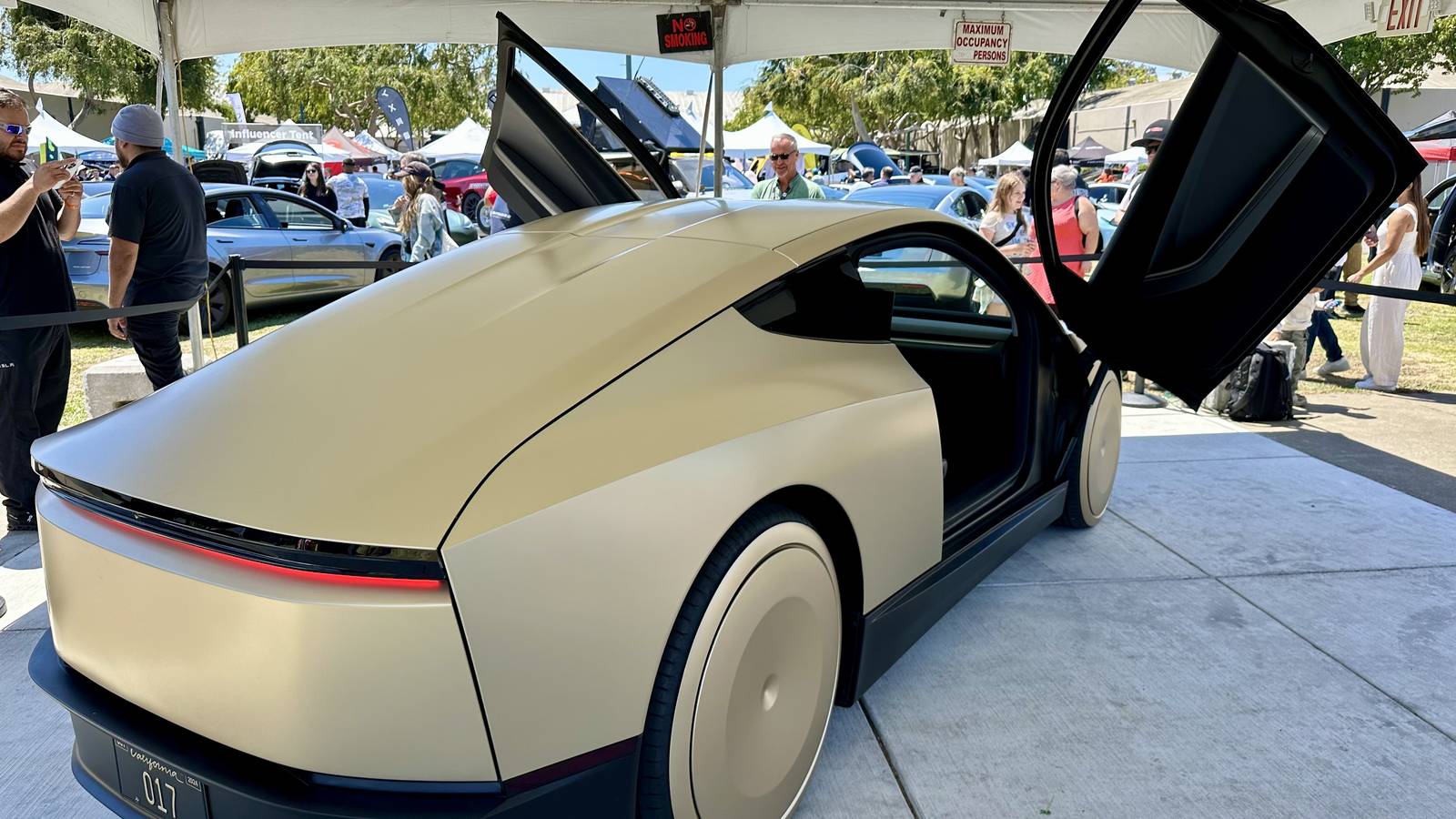 A gold Tesla Cybercab with its butterfly doors open on display under a white tent in San Mateo, California